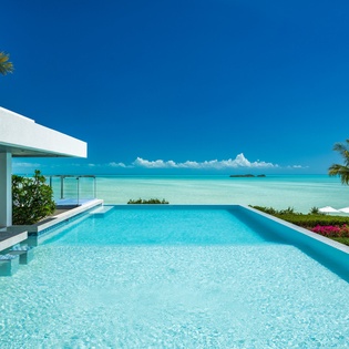A pristine infinity pool perfectly frames turquoise waters and tropical palms, creating your private slice of paradise under vibrant blue skies.