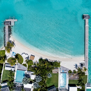 Aerial view showcasing pristine turquoise waters and white sand beach with twin piers extending into crystal-clear tropical waters.