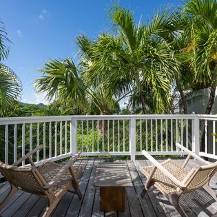 Soak up tropical vibes on your private deck where swaying palms frame blue skies and wicker chairs invite peaceful morning coffee moments.