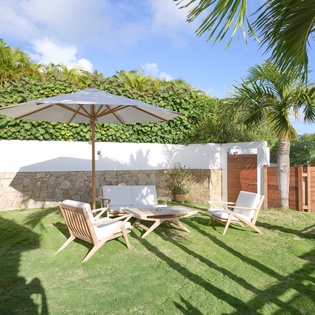 Your private tropical garden oasis awaits with comfortable seating under shade, surrounded by lush palms and greenery for ultimate relaxation.