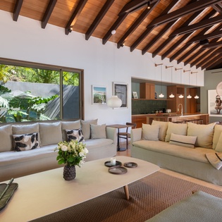 Sink into plush seating beneath stunning wood beams as tropical views frame your perfect retreat through floor-to-ceiling windows.