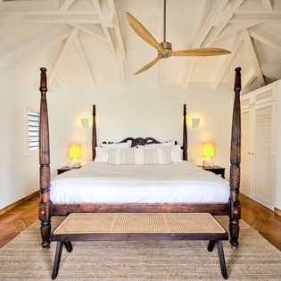 Drift off under vaulted ceilings and a gentle ceiling fan in your beautifully appointed bedroom, where elegant four-poster details and warm bedside lighting create a peaceful island retreat.