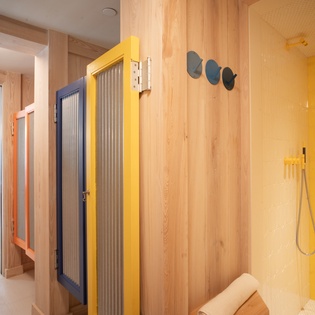 Unwind in your private wellness sanctuary featuring a vibrant yellow shower and rejuvenating sauna with natural wood finishes.