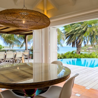 Dine beneath elegant lighting as palm trees frame stunning infinity pool and sea views beyond, creating an idyllic tropical escape setting.