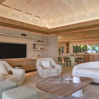 Your sophisticated living space flows seamlessly into the kitchen, featuring warm wood tones, plush seating, and soaring vaulted ceilings that create an airy, luxurious retreat.