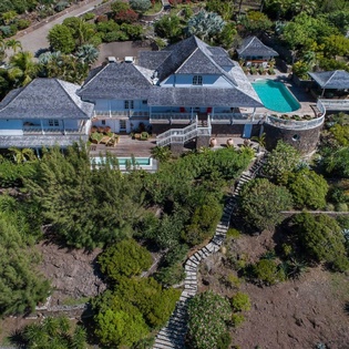 Aerial view of a spacious tropical villa nestled among lush hillside gardens, with multiple pools and terraces overlooking the surrounding landscape.