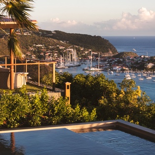 Stunning Caribbean vista from this hillside property showcases dramatic coastline, sailboat-filled harbor, and lush tropical landscape at golden hour.