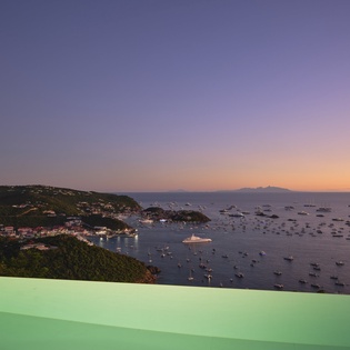 Stunning coastal sunset view over the harbor with boats dotting the serene waters below rolling green hills.