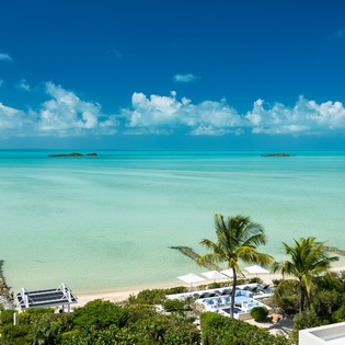 Stunning aerial view of a pristine beachfront property surrounded by turquoise waters, lush palms, and private white-sand shores—a tropical paradise setting.