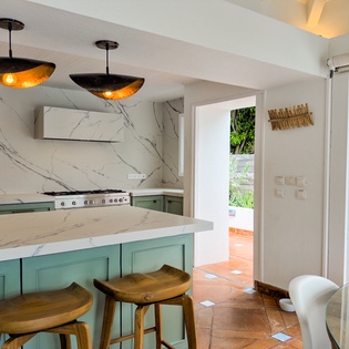 This elegant kitchen features marble countertops, custom cabinetry, and a gas range—perfect for preparing meals during your stay. Natural light streams through open doorways leading to the garden.