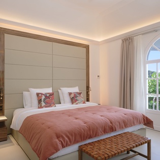 Sink into luxury with this elegant bedroom featuring warm coral bedding, ambient lighting, and French doors opening to lush greenery.