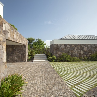 Modern stone-clad architecture seamlessly blends with landscaped grounds featuring geometric paving patterns and lush greenery throughout the property exterior.