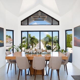 Gather at this elegant dining table, where vaulted ceilings and tropical views through floor-to-ceiling windows create the perfect backdrop for your morning coffee or evening meals with loved ones.