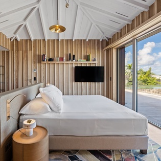 Your serene bedroom features soaring vaulted ceilings, warm wood accents, and floor-to-ceiling windows framing tropical mountain views from your private terrace.