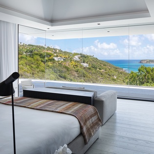 Wake up to breathtaking turquoise waters and lush hillside views from your bed in this stunning oceanfront bedroom.
