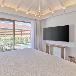 Drift off in your serene bedroom featuring exposed beams, modern TV, and tranquil pool views through floor-to-ceiling windows.