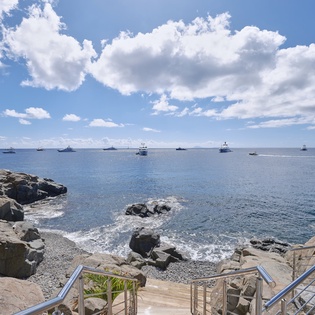 Dramatic rocky coastline with crystal-clear waters and distant boats creates a stunning natural backdrop for this waterfront location.