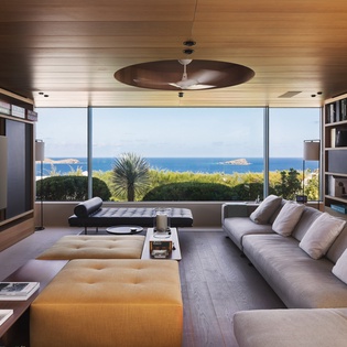 Unwind in your sophisticated living room with floor-to-ceiling windows framing breathtaking ocean views, plush seating, and a curated library.