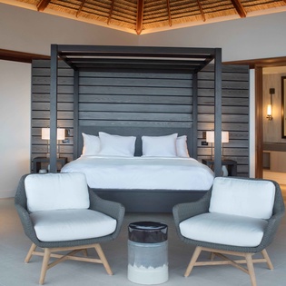 Your spacious suite blends modern luxury with tropical charm, featuring a stunning four-poster bed and cozy seating area under soaring wooden beams.