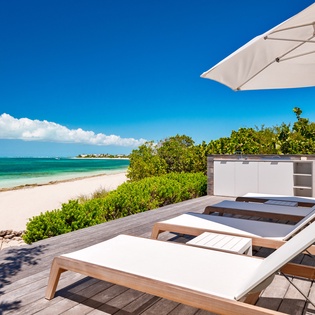 Beachfront deck with premium loungers positioned steps from pristine white sand and turquoise waters.