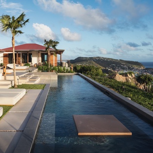 Spectacular infinity pool overlooking dramatic coastal cliffs and harbor views, with modern villa architecture set in tropical landscaping.