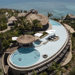 Stunning beachfront resort featuring an infinity pool with swim-up bar, surrounded by tropical palms and crystal-clear ocean views.