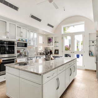 A bright, fully-equipped kitchen with granite counters and high-end appliances awaits your culinary adventures. Sunlight pours through arched windows, illuminating a spacious island and elegant white cabinetry—perfect for preparing meals in style.