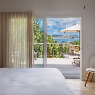 Step into your serene bedroom where crisp white linens meet stunning sea views, and the private balcony invites you to unwind with gentle island breezes and endless blue horizons.