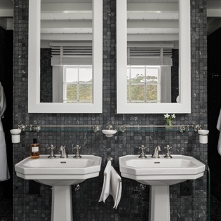 Indulge in luxury with dual pedestal sinks, plush robes, and elegant dark tile creating your perfect morning routine.