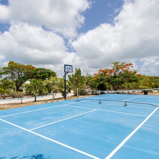 Bright blue sport courts nestled among tropical trees under fluffy clouds provide the perfect setting for friendly competition and outdoor fun during your stay.