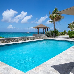 Crystal-clear pool overlooking turquoise Caribbean waters, framed by swaying palms and a covered gazebo—your private oasis for sun-soaked relaxation.