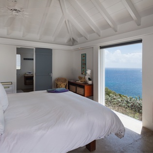 Wake up to breathtaking ocean panoramas framed by your bedroom window, where white linens meet endless blue horizons and vaulted ceilings invite relaxation.