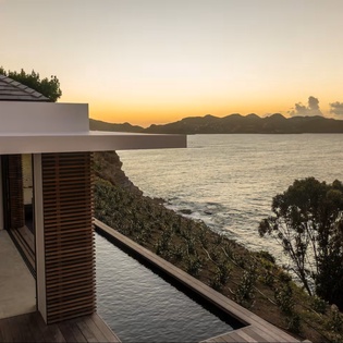Modern terrace overlooking tranquil waters and distant islands as the sun sets, bathing the scene in warm golden light.
