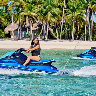 Tropical paradise beach with crystal-clear waters, pristine white sand, and swaying palm trees offering the perfect backdrop for water sports adventures.