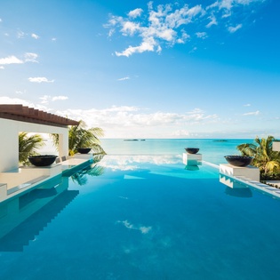 This luxury retreat features a stunning infinity pool set against pristine turquoise waters, surrounded by modern tropical architecture and swaying palms—the perfect backdrop for a serene escape.