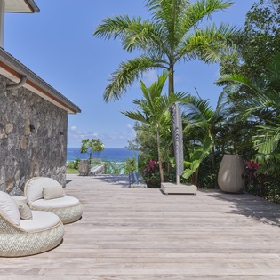 Luxurious stone villa terrace with ocean views, surrounded by tropical palms and designer seating for ultimate relaxation.
