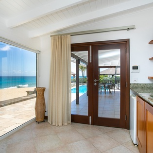 Step into your kitchenette where floor-to-ceiling windows frame stunning turquoise waters and pristine sand just steps away—your private beachfront paradise awaits.