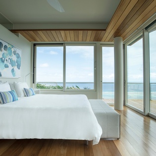 Wake up to breathtaking ocean views from your serene bedroom, where natural light floods through floor-to-ceiling windows and peaceful waves await just outside.