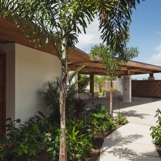 Modern tropical architecture with wooden accents and lush landscaping creates an inviting entrance to this contemporary vacation property.