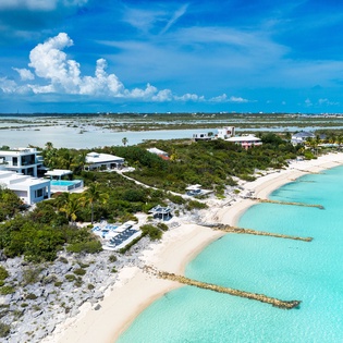 Aerial view of beachfront vacation villas nestled amid tropical vegetation along pristine turquoise waters and white sand beaches.