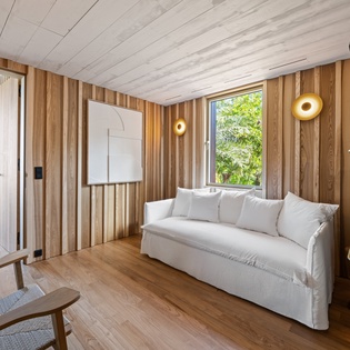 Relax in your serene living space where warm wood meets modern comfort, featuring a plush white sofa and peaceful garden views.