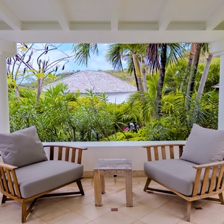 A tranquil covered terrace framed by swaying palms and tropical greenery, offering peaceful ocean glimpses and a private sanctuary to unwind beneath the Caribbean sky.