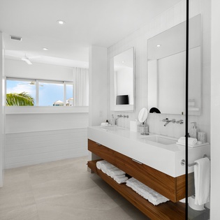 Step into your sleek bathroom sanctuary where marble meets warm wood, fresh towels await, and ocean glimpses through the window promise paradise.