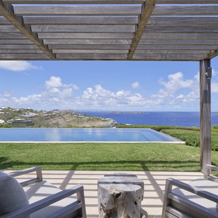 An inviting outdoor lounge framing expansive ocean views and coastline, with comfortable seating and a sparkling infinity pool just steps away.