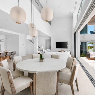 Dine in style at your elegant open-concept space, where modern pendant lights illuminate gatherings and glass doors reveal tropical paradise beyond.