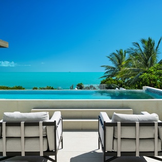 Stunning infinity pool terrace with panoramic ocean views and tropical palm trees in paradise setting.