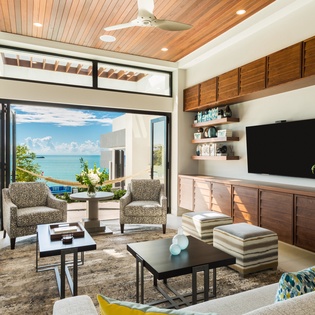 Sink into plush seating in your sunlit living room where folding glass doors frame stunning turquoise sea views and blend indoor luxury with the tropical breeze outside.