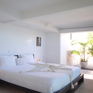 Wake up to crisp white linens and natural light streaming through your private balcony doors, overlooking tropical greenery.