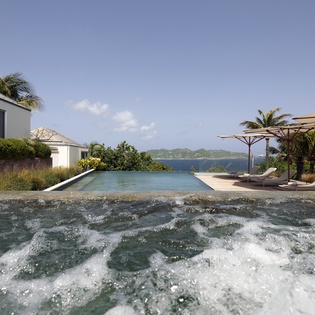 Modern villa with infinity pool overlooking tropical waters, complete with loungers and umbrellas for the ultimate escape.