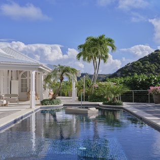 Elegant white villa with pristine pool nestled among tropical palms and lush hillsides under Caribbean blue skies.